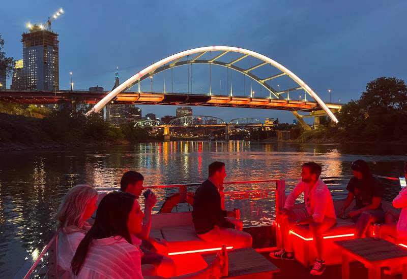 people glowing in red light on a sunset boat cruise with nashville skyline behind
